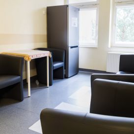 Poczekalnia — ciemne fotele i stolik przy oknie z widokiem na zieleń
